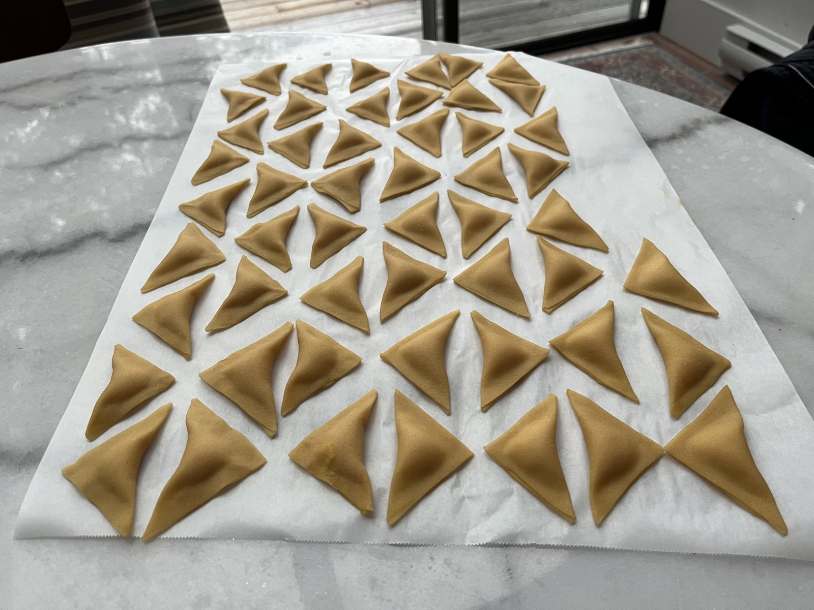 Freshly folded triangle agnolotti resting on parchment.
