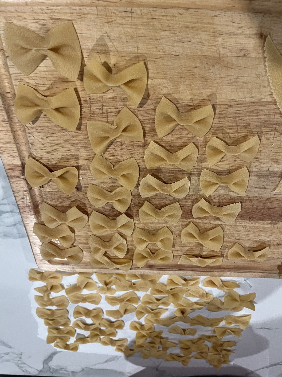 Hand-pinched farfalle bow ties on a wooden cutting board.