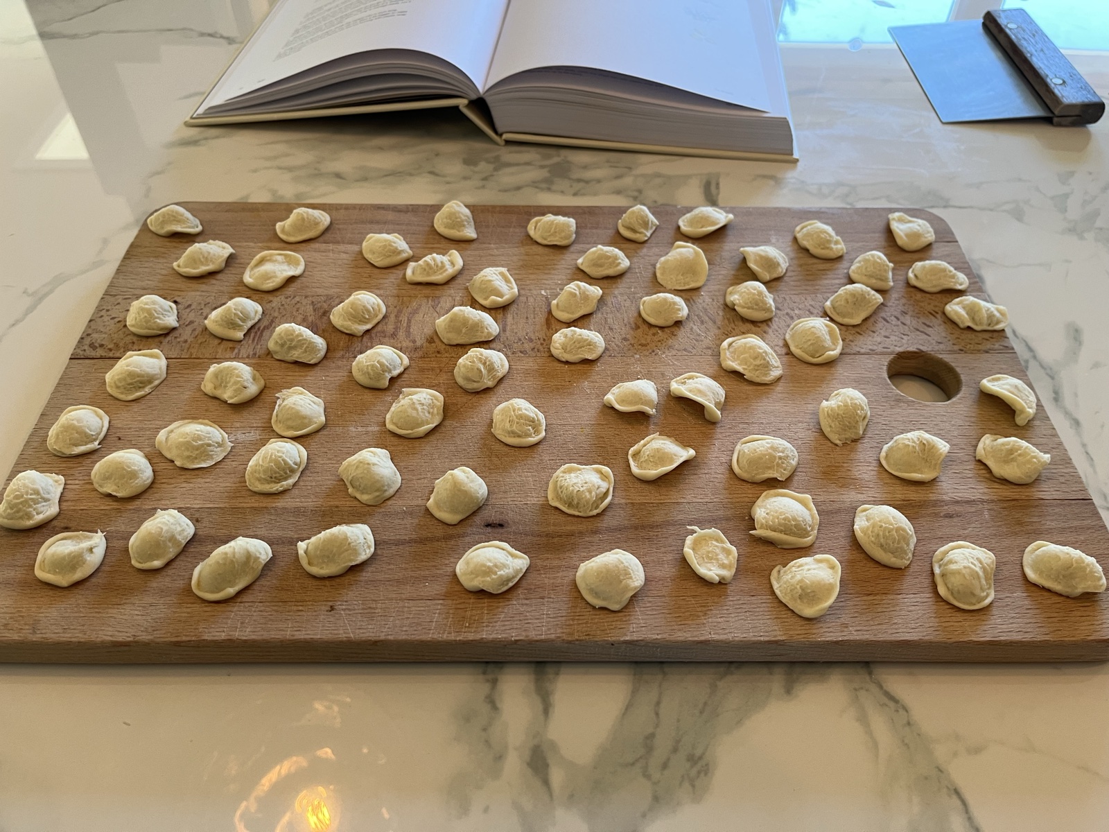 Orecchiette pressed by hand on a wooden board, with a cookbook in the background.