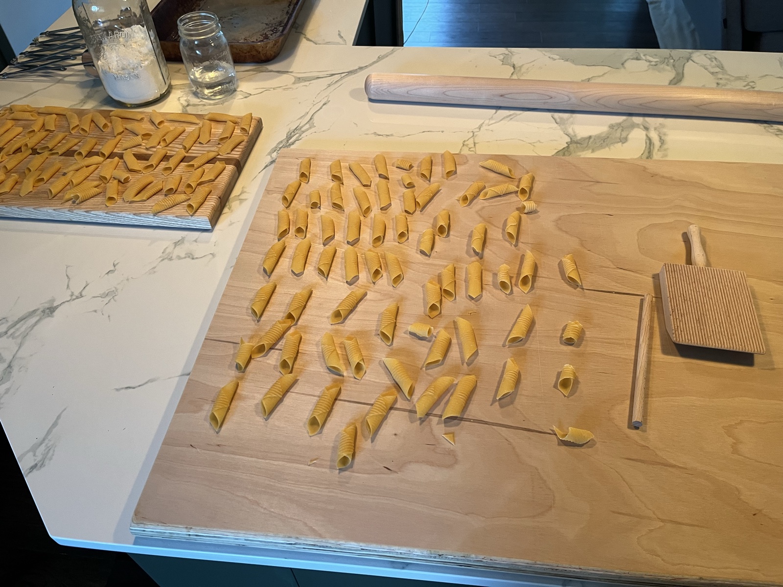 Hand-rolled garganelli being shaped on a wooden gnocchi board with a rolling pin.