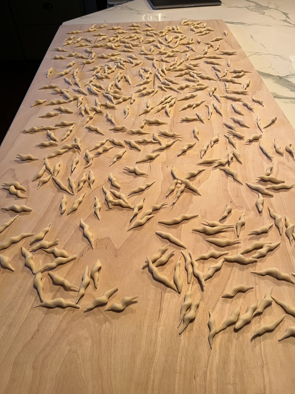 A large wooden board covered in hundreds of hand-rolled trofie in warm evening light.