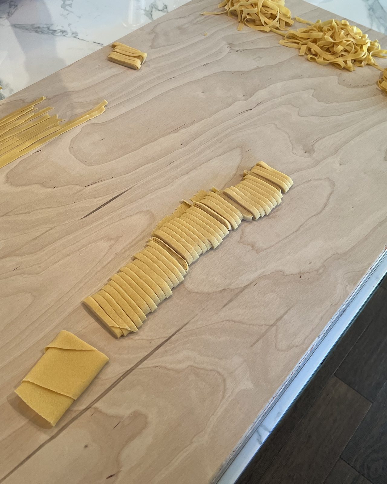 Fresh tagliatelle being cut by hand on a wooden board during a pasta lesson.