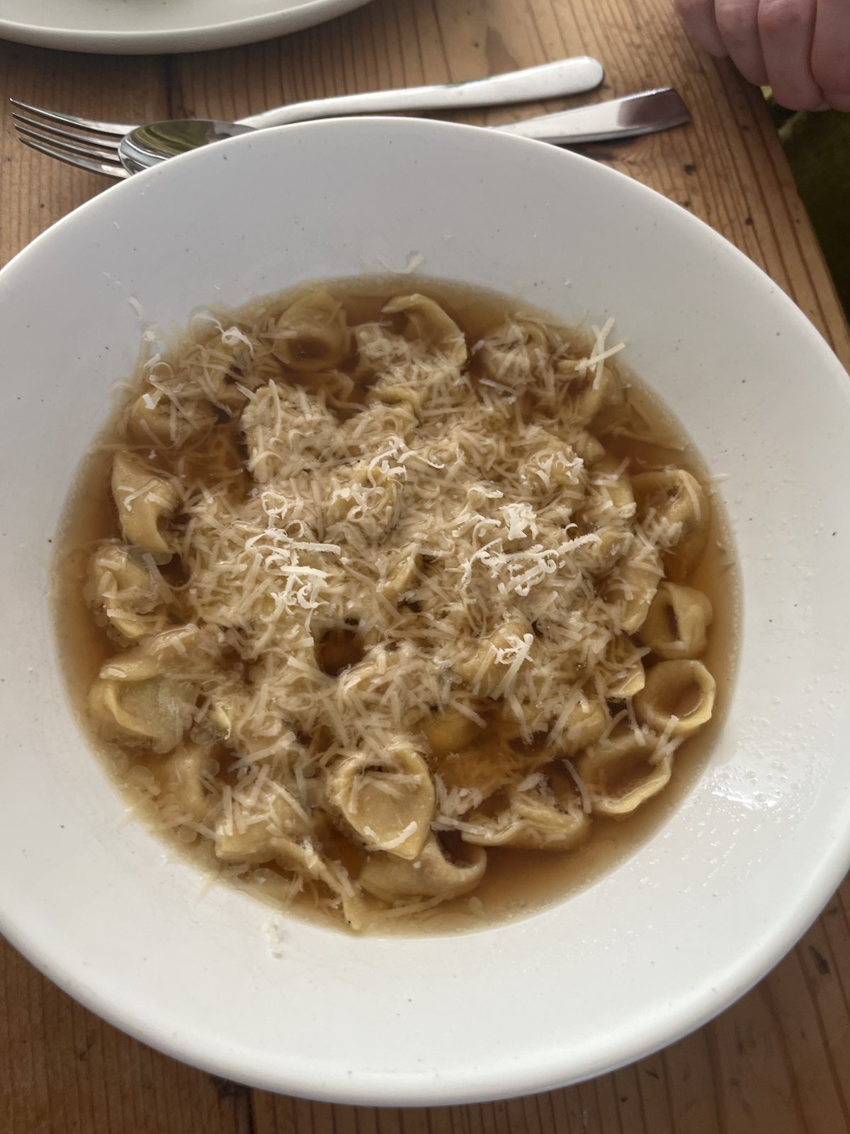 Bowl of handmade tortellini in brodo topped with grated parmesan, served at the table.